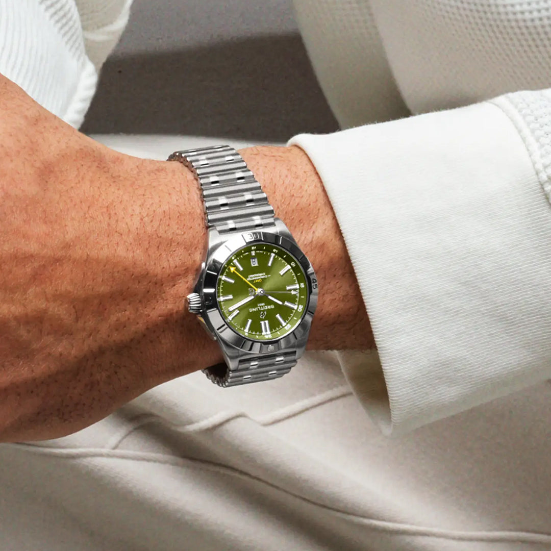 A person wearing the limited edition BREITLING Chronomat Automatic GMT 40 Giannis Antetokounmpo wristwatch with a silver metallic band and green dial, paired with a white textured long-sleeve shirt, reflecting an elegance similar to Giannis Antetokounmpo's off-court style.
