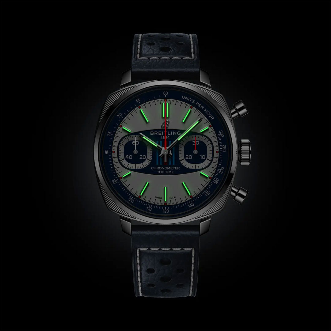 The Breitling Top Time B01 Racing is a luxury chronograph wristwatch with a black strap, luminous green markers, Martini Racing red accents, subdials, and three pushers—all set against a sleek black background.