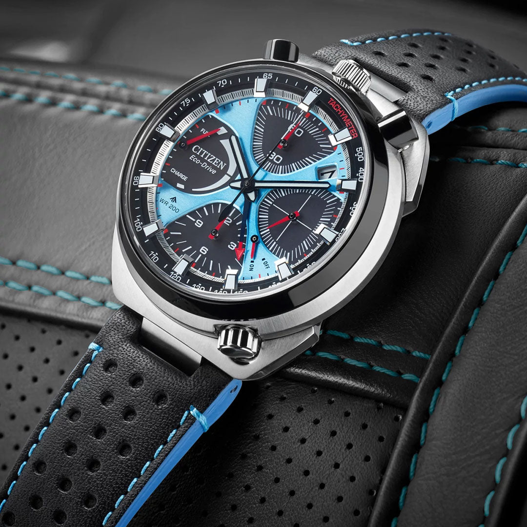 The CITIZEN Promaster Tsunoc Chrono Racer Limited Edition Eco-Drive 44.5mm Watch features a blue and black dial with red accents, three subdials, and sits on perforated black leather with blue stitching and edges.