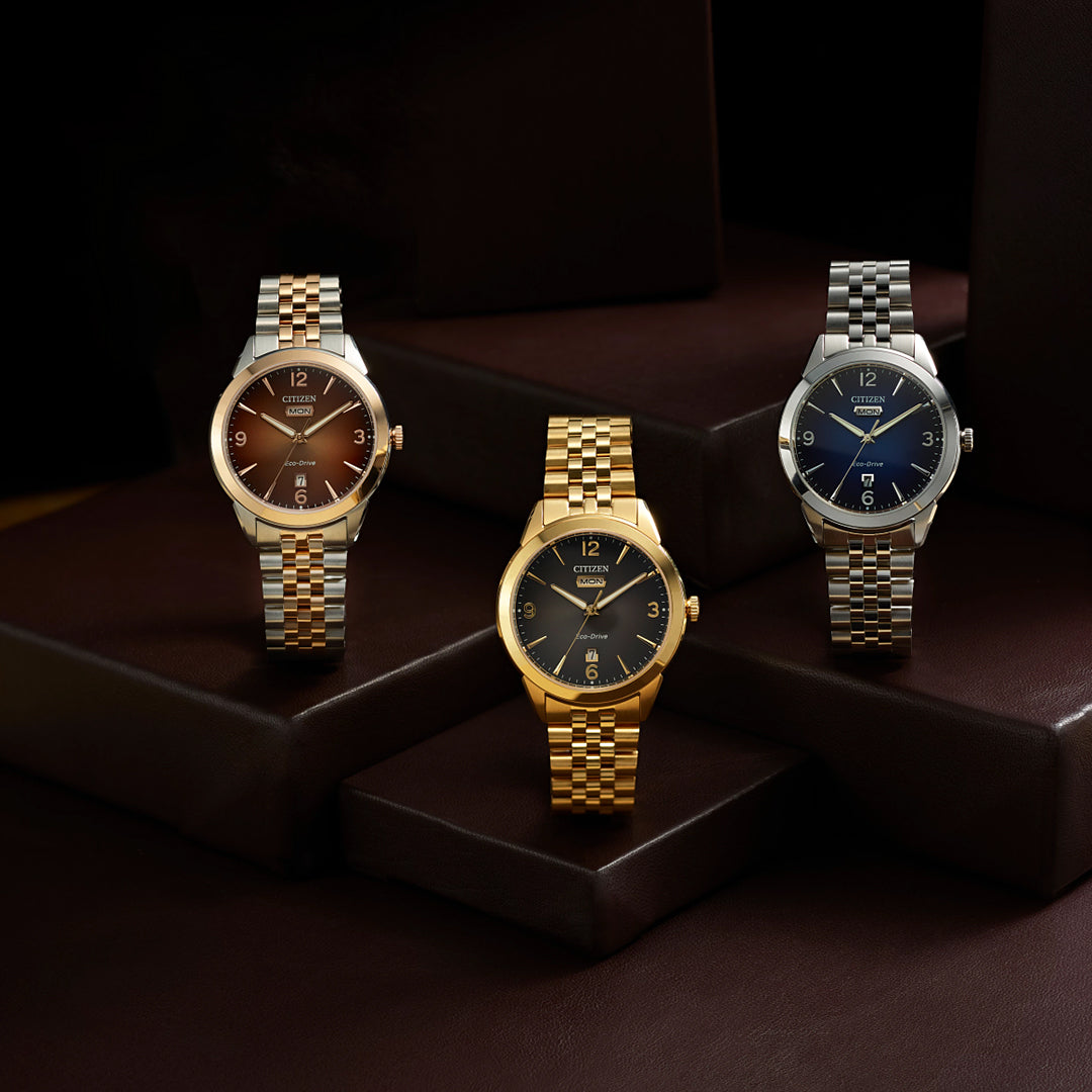 On display are three CITIZEN Rolan Eco-Drive 40.5mm watches, each featuring a distinct metal bracelet and round face. One is gold-toned, another is silver with a blue face, and the third combines silver and gold with a brown face.
