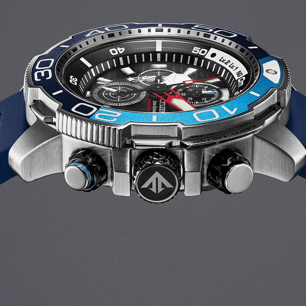 Close-up of the luxurious CITIZEN Promaster Aqualand Eco-Drive 46mm Watch, showcasing its blue and silver rotating bezel, prominent pushers, and textured crown. The watch face features subdials and bold hour markers against a blue strap on a gray background, all powered by Eco-Drive technology.