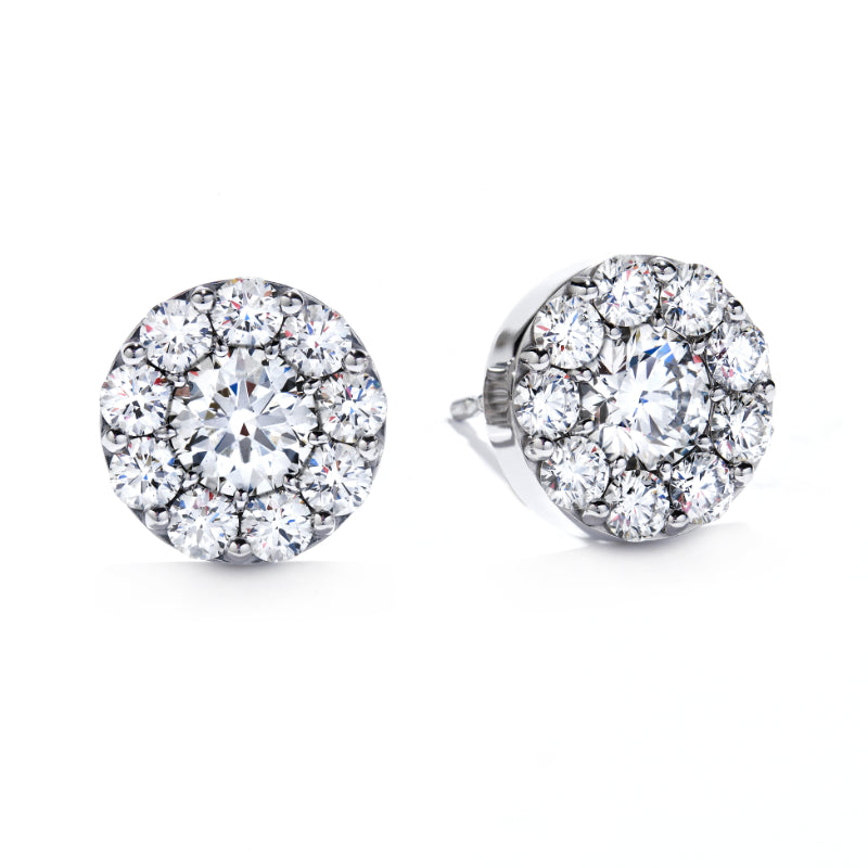 Introducing the Hearts On Fire Fulfillment Stud Earrings: These exquisite round diamond cluster stud earrings are set in lustrous white gold and feature a stunning central diamond encircled by smaller diamonds, forming a dazzling halo effect. Perfect for those who appreciate the brilliance and precision synonymous with Hearts on Fire craftsmanship.
