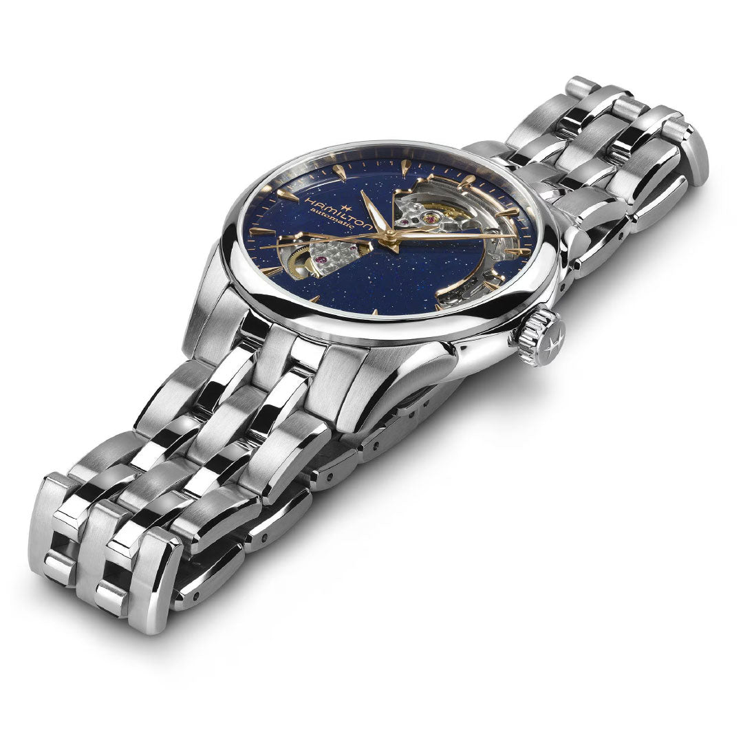 The Hamilton Jazzmaster Open Heart Lady Auto 36mm, a silver stainless steel dress watch with a deep blue open-worked dial, gold-tone markers, automatic movement, and multi-link bracelet by Hamilton Watch, rests on a white surface.