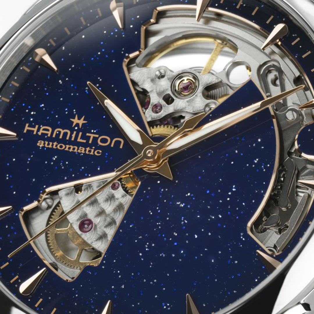 Close-up of the Hamilton Jazzmaster Open Heart Auto 36mm by Hamilton Watch, showcasing a blue star-speckled dial, rose gold hands, and exposed H-10 automatic movement with gold and silver details.