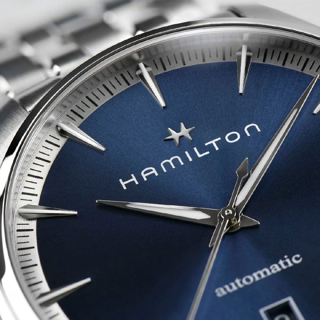 Close-up of the Hamilton Jazzmaster Auto 40mm Watch by Hamilton Watch, featuring a metallic blue dial, silver hour markers and hands, "automatic" on the lower dial, with part of the stainless steel bracelet visible.