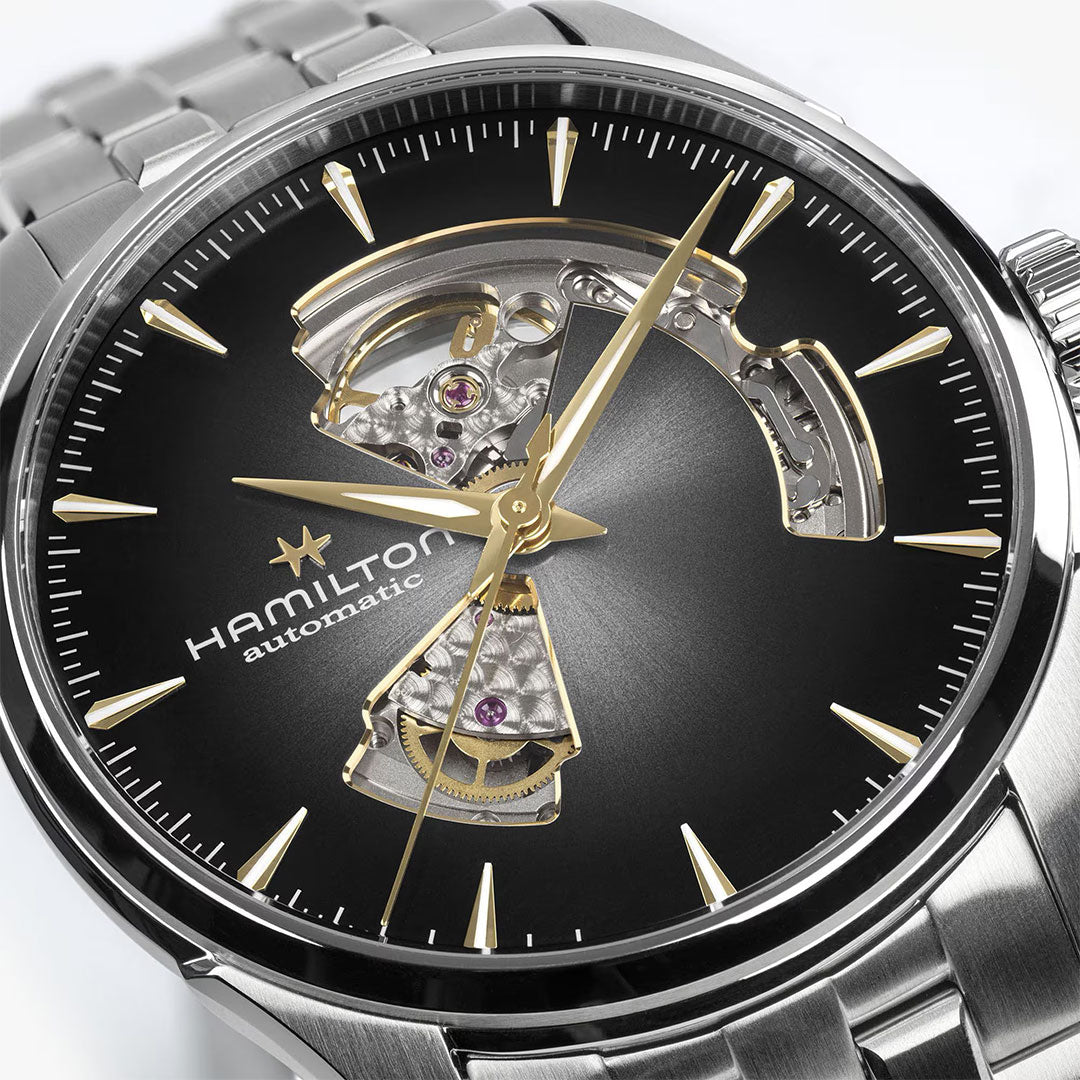 Close-up of the Hamilton Jazzmaster Open Heart Auto 42mm Watch by Hamilton Watch, featuring a black and gold skeleton dial with visible gears, gold-tone hands and hour markers, and a stainless steel bracelet.
