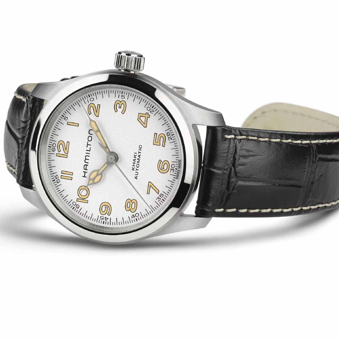 The Hamilton Khaki Field Murph Auto 38mm Watch by Hamilton Watch features a silver case, white dial with gold Arabic numerals, black hands, and a black leather strap with white stitching, displayed at an angle.