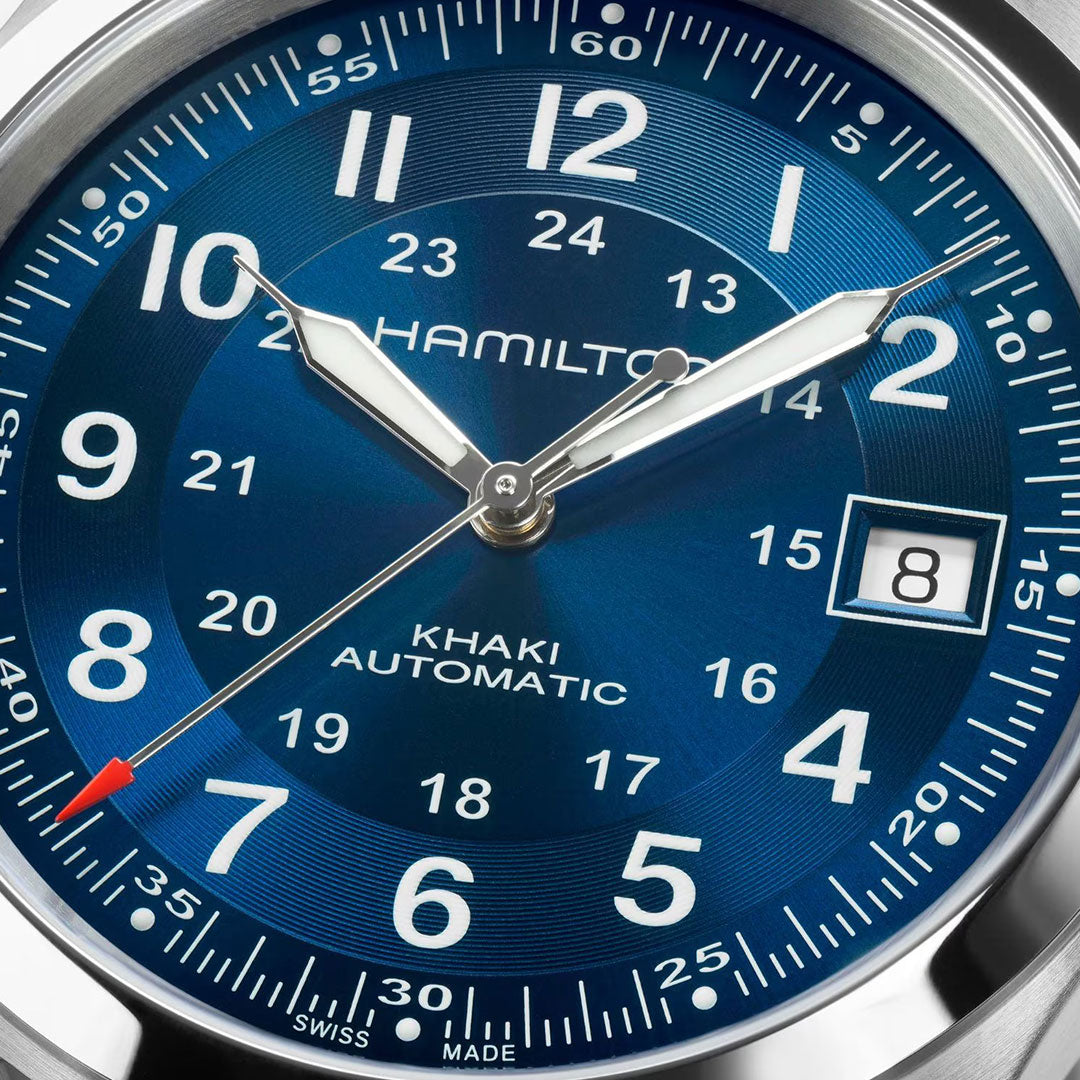 Close-up of the Hamilton Khaki Field Auto 38mm Watch by Hamilton Watch, featuring a blue dial with both 12-hour and 24-hour markers, a date window displaying "8," silver hour and minute hands, and a red-tipped second hand reflecting its military design.