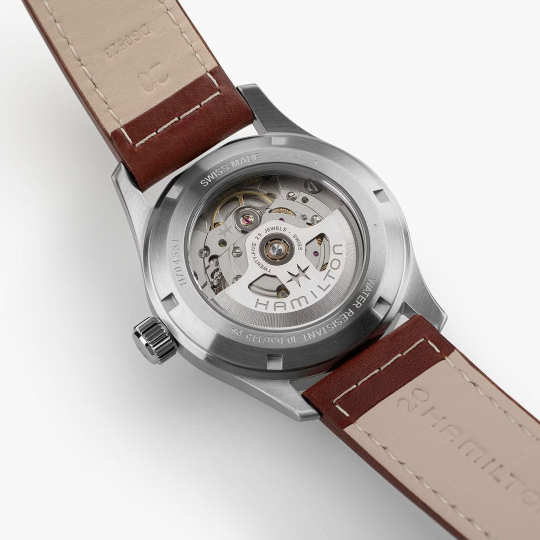 A close-up of the Hamilton Khaki Field Auto 38mm Watch by Hamilton Watch shows its transparent case back, revealing the H-10 automatic movement and brown leather strap with beige lining, highlighting its military-inspired heritage.