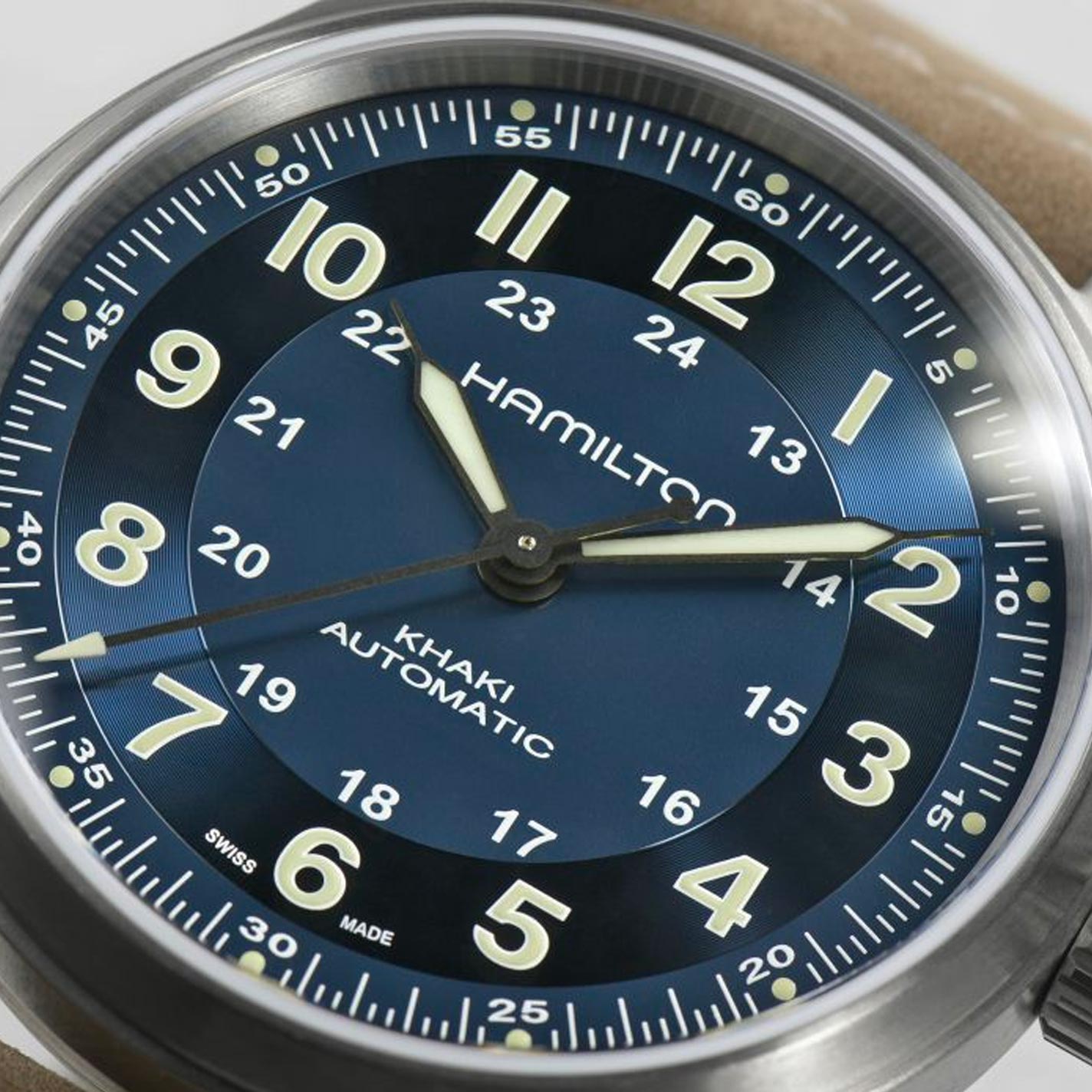 The Hamilton Khaki Field Titanium Auto 42mm Watch features an eye-catching blue dial adorned with large luminous Arabic numerals, a date display, and prominent hands. Emphasizing Hamilton's military legacy, this watch includes an impressive 80-hour power reserve and is encased in stainless steel with a beige leather strap.