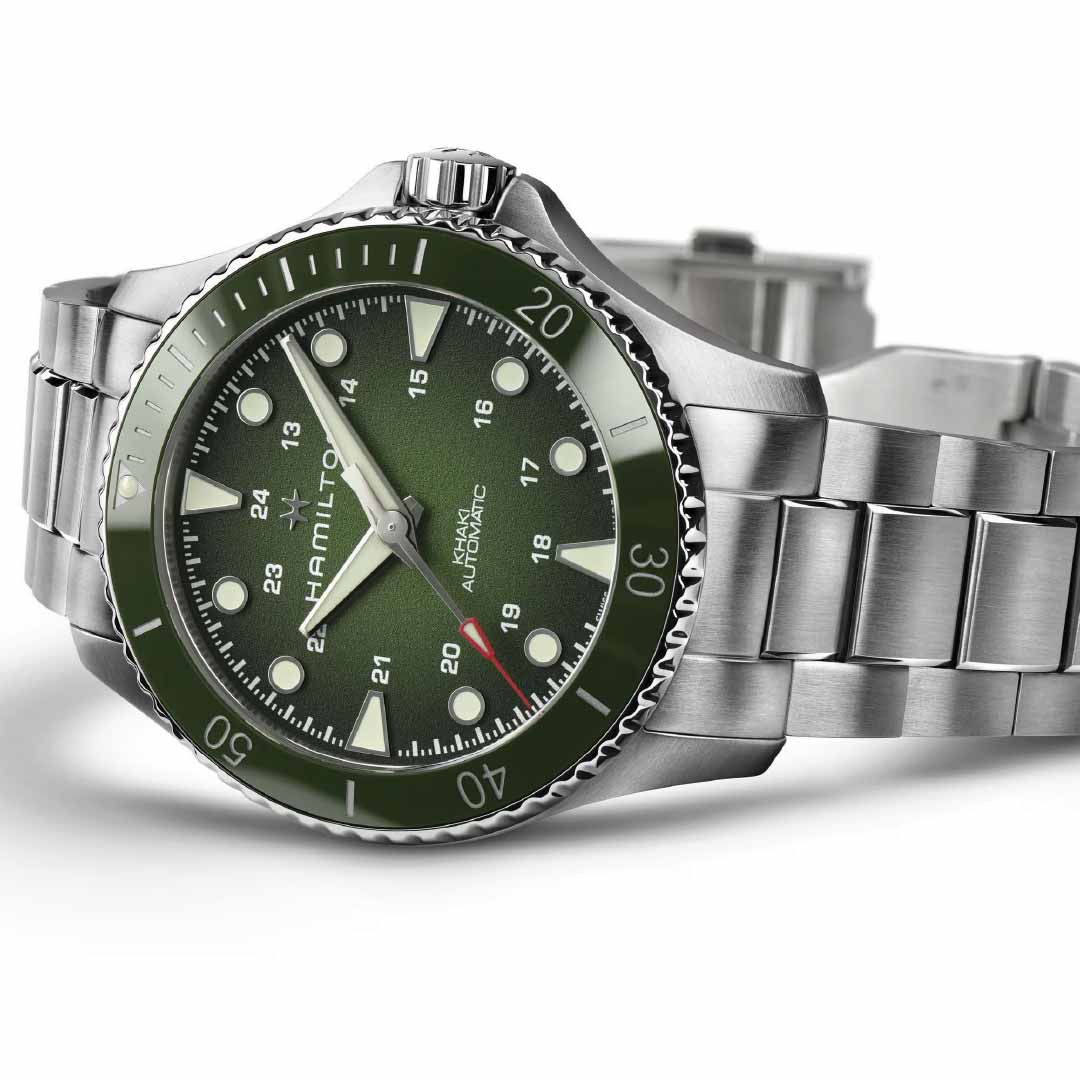 A close-up of the Hamilton Khaki Navy Scuba Auto 43mm Watch by Hamilton Watch, featuring a green dial, silver hour markers, H-10 automatic movement, stainless steel band, green ceramic bezel, and 12/24-hour time formats.