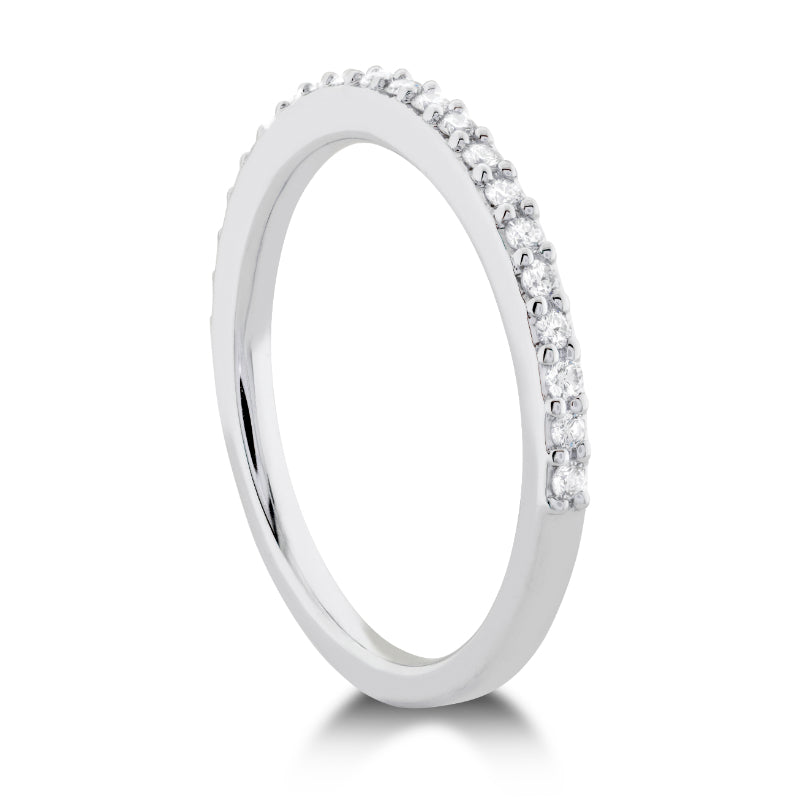 The Hearts On Fire Camilla Anniversary Ring, crafted from 18K white gold, showcases small, sparkling round brilliant diamonds embedded along the top half against a white background. This sleek and elegant ring perfectly embodies the timeless beauty of Hearts on Fire designs.