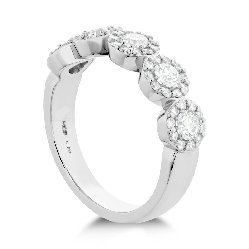 The Hearts On Fire Fulfillment 18K White Gold Round Brilliant Diamond Anniversary Ring, made by Hearts on Fire, showcases a collection of five round diamond clusters set along the band. Each cluster is surrounded by smaller diamonds that enhance its sparkling appearance. This exquisite piece of luxury diamond jewelry is elegantly positioned at an angle against a plain white background.
