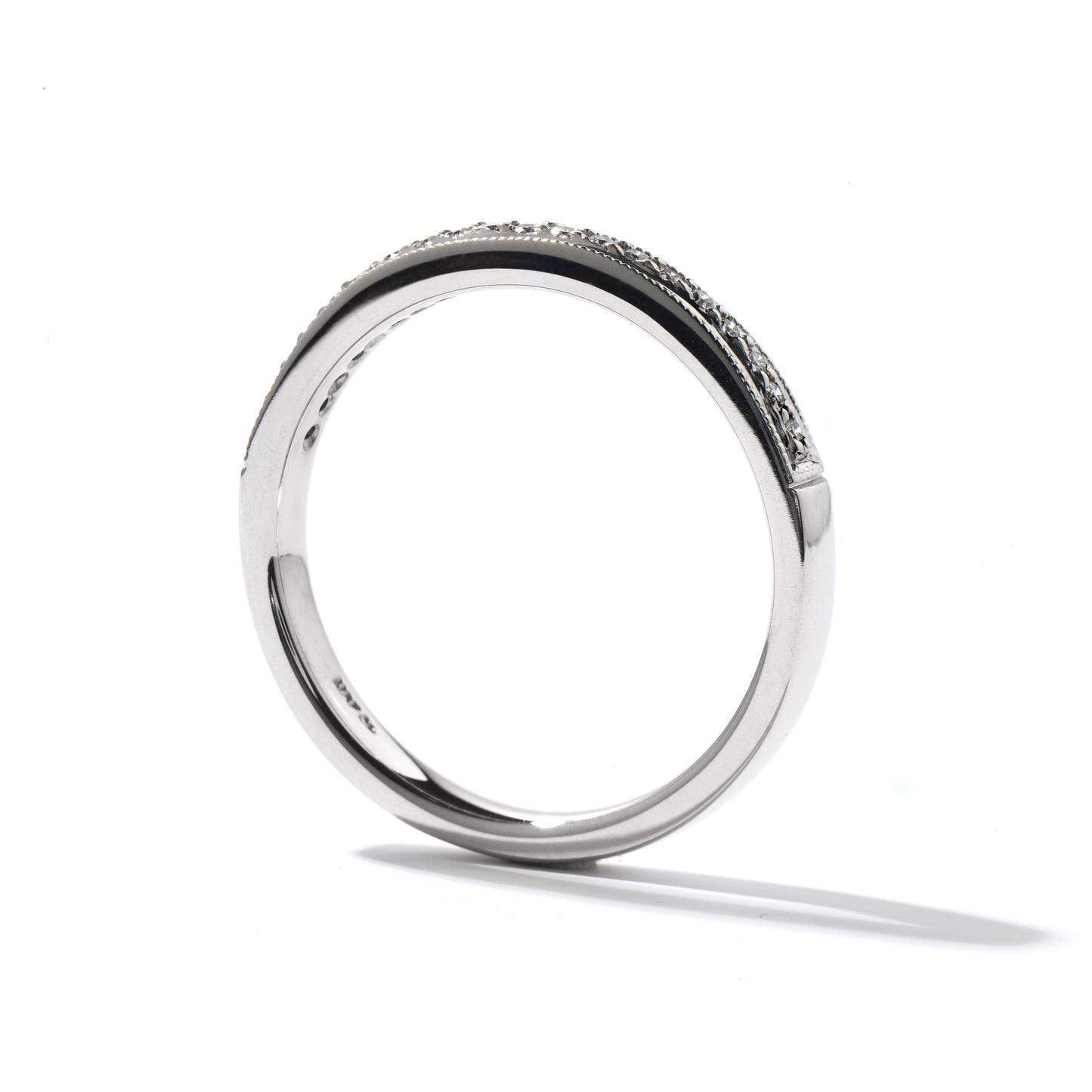 The Hearts On Fire Platinum Round Brilliant Diamond Anniversary Ring is beautifully displayed, showcasing a smooth, polished finish with a row of round diamonds adorning the top half. Positioned upright on a white surface, it casts a gentle shadow, embodying the signature elegance of Hearts on Fire.