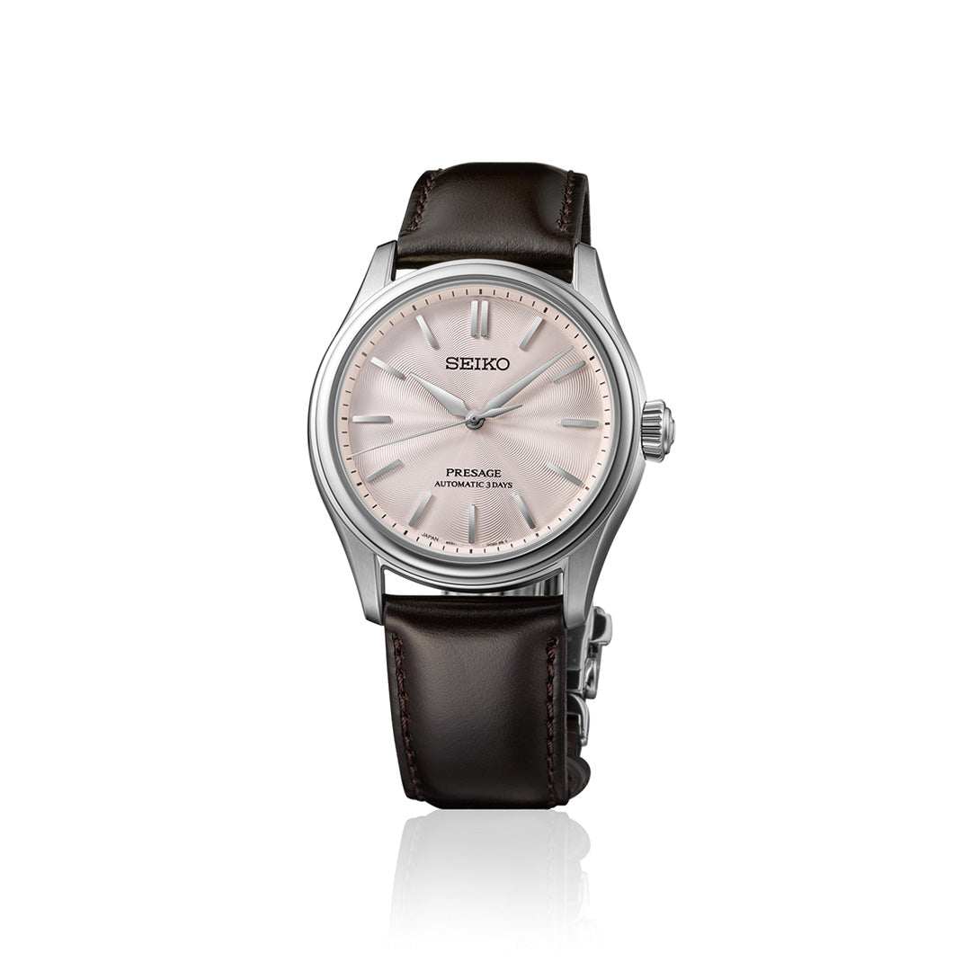 The Seiko Presage Classic Series Automatic 38mm Watch by Seiko features a light pink dial, silver hour markers, and a brown leather strap, shown against a white background.