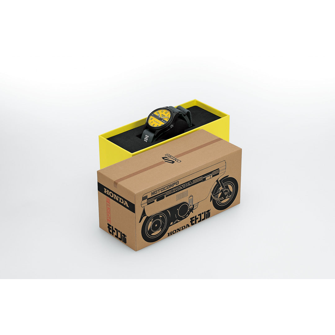 A Seiko 5 Sports Field Series MOTOCOMPO Limited Edition Automatic 36.37mm watch by Seiko, featuring a yellow dial, is displayed in a yellow and black presentation box. The 36.37mm watch box is partially enclosed within an outer cardboard sleeve decorated with black illustrations of a motorcycle engine and wheels, along with the Honda logo and Japanese text.