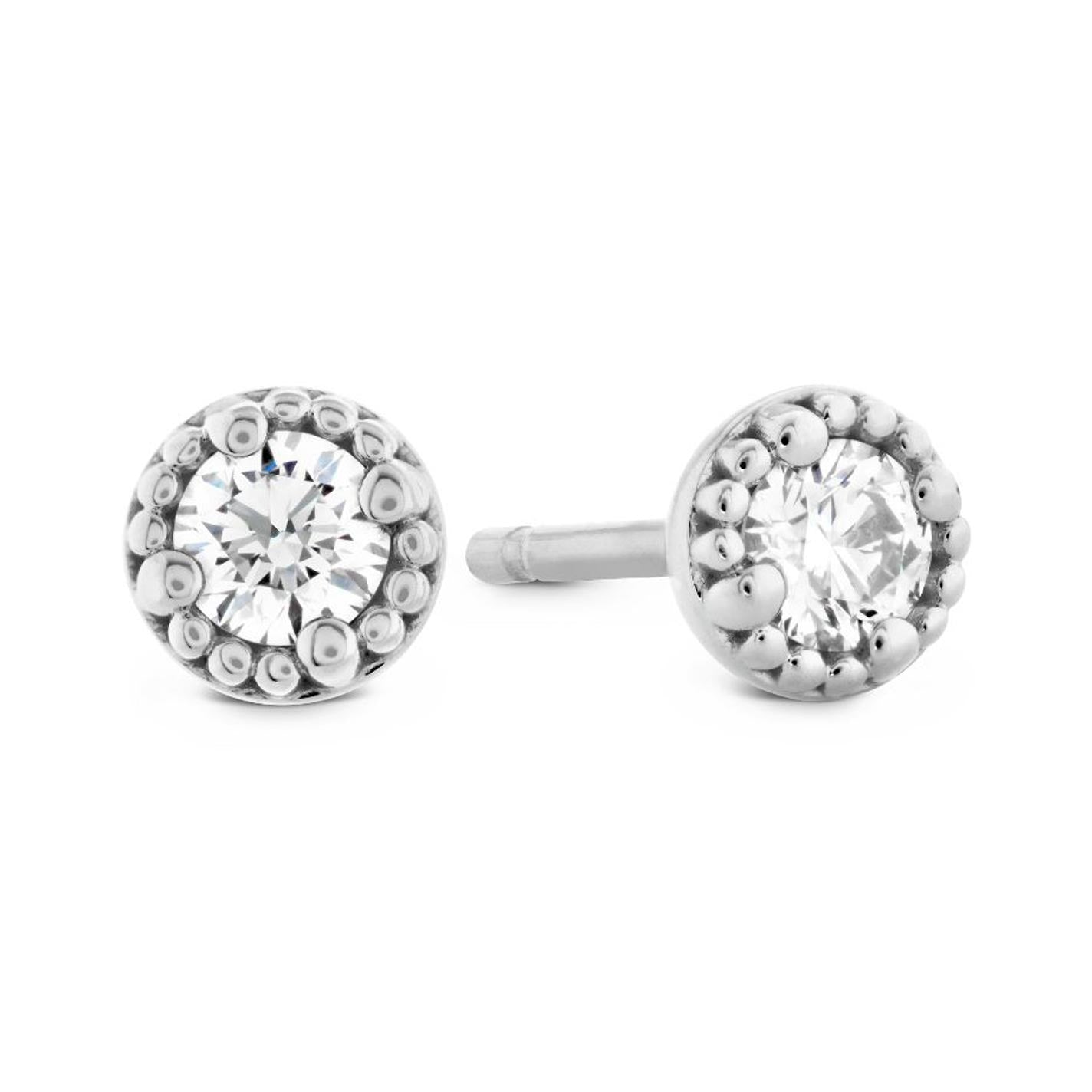 The Hearts On Fire Liliana Milgrain Stud Earrings feature a pair of exquisite silver studs, each accented with a round, sparkling gemstone at the center. These earrings are elegantly surrounded by a decorative border of small metallic beads, adding an exquisite touch.