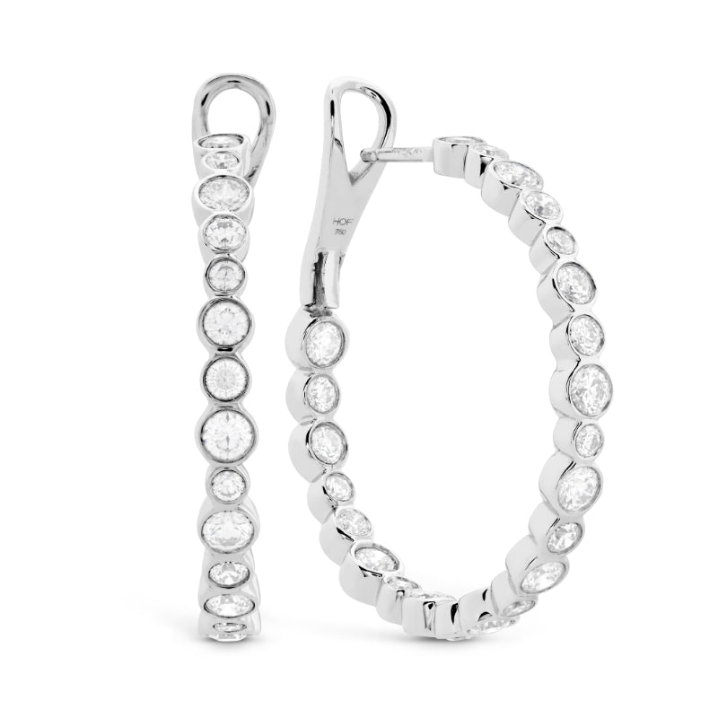 The Hearts On Fire Hoop Earrings from Hearts on Fire, featuring a sleek row of sparkling round diamonds set in white gold, capture the essence of luxurious elegance. Positioned upright against a white background, they perfectly highlight their sophisticated design.