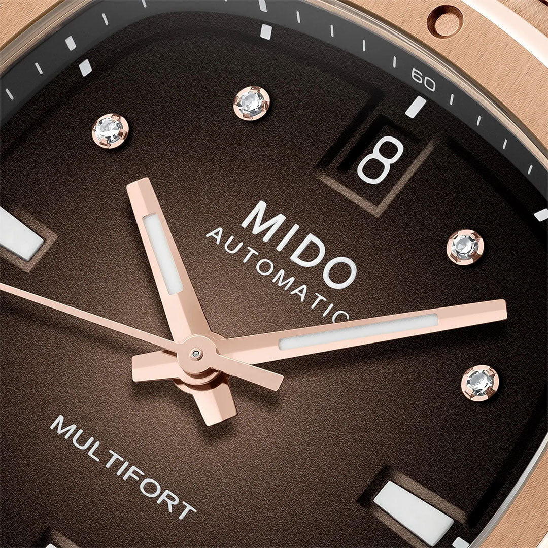 Close-up of the MIDO Multifort TV 35 Automatic 35mm watch with rose gold hands, diamond hour markers, date window at 3 o’clock, and a Nivachron balance spring. Brown background highlights its modern appeal.