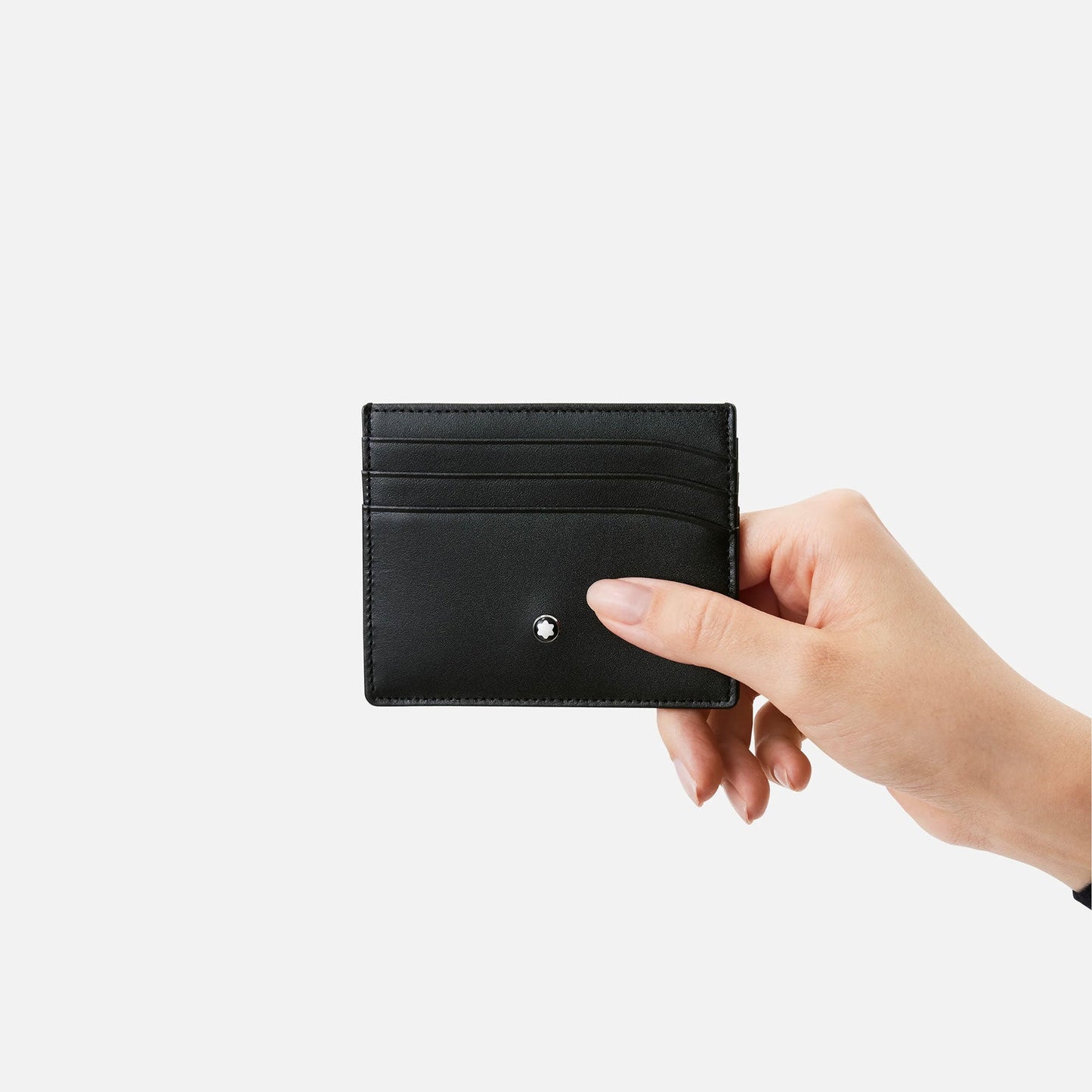 A hand elegantly holds the Montblanc Meisterstuck Pocket 6cc Leather Card Holder against a plain white backdrop. This accessory from Montblanc, crafted from full-grain calfskin, features several slots with refined stitching details and a subtle metallic logo at the bottom center, capturing timeless sophistication.