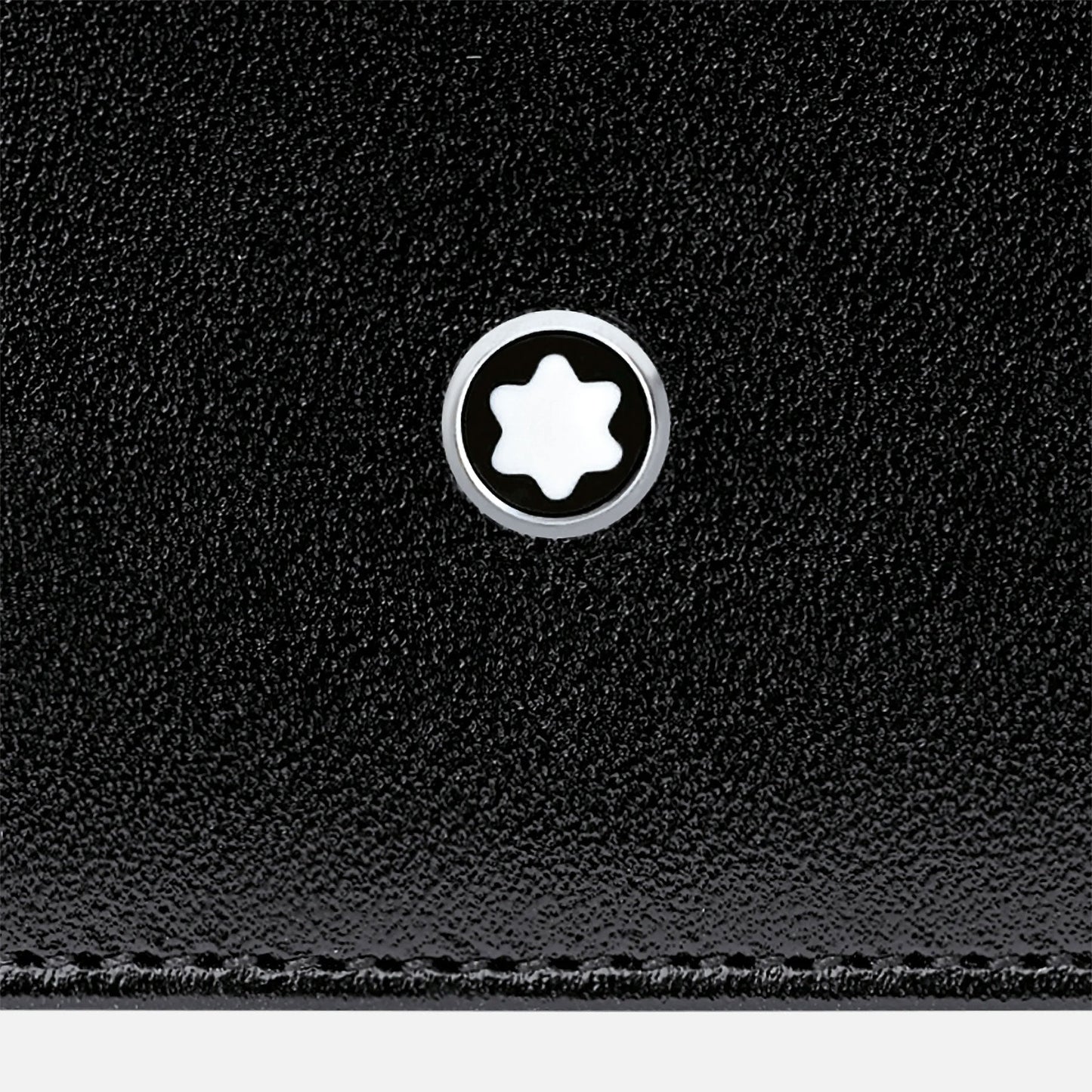Close-up of the Montblanc Meisterstück Pocket 6cc Leather Card Holder's black calfskin leather surface with a circular logo. The logo displays a white six-pointed star inside a black circle, outlined with silver, reflecting a minimalist and elegant design characteristic of the esteemed Meisterstück collection by Montblanc.