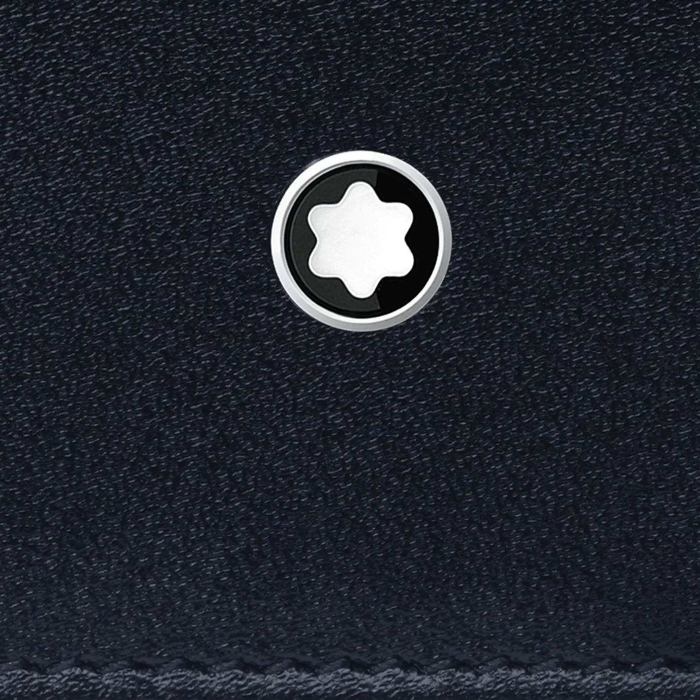 Close-up of the textured black leather surface of the Montblanc Meisterstuck Pocket 6cc Leather Card Holder, featuring a small circular emblem. The emblem includes a white six-pointed star within a black circle, offering a contrasting and elegant design. This lightweight Montblanc accessory perfectly combines style and function.