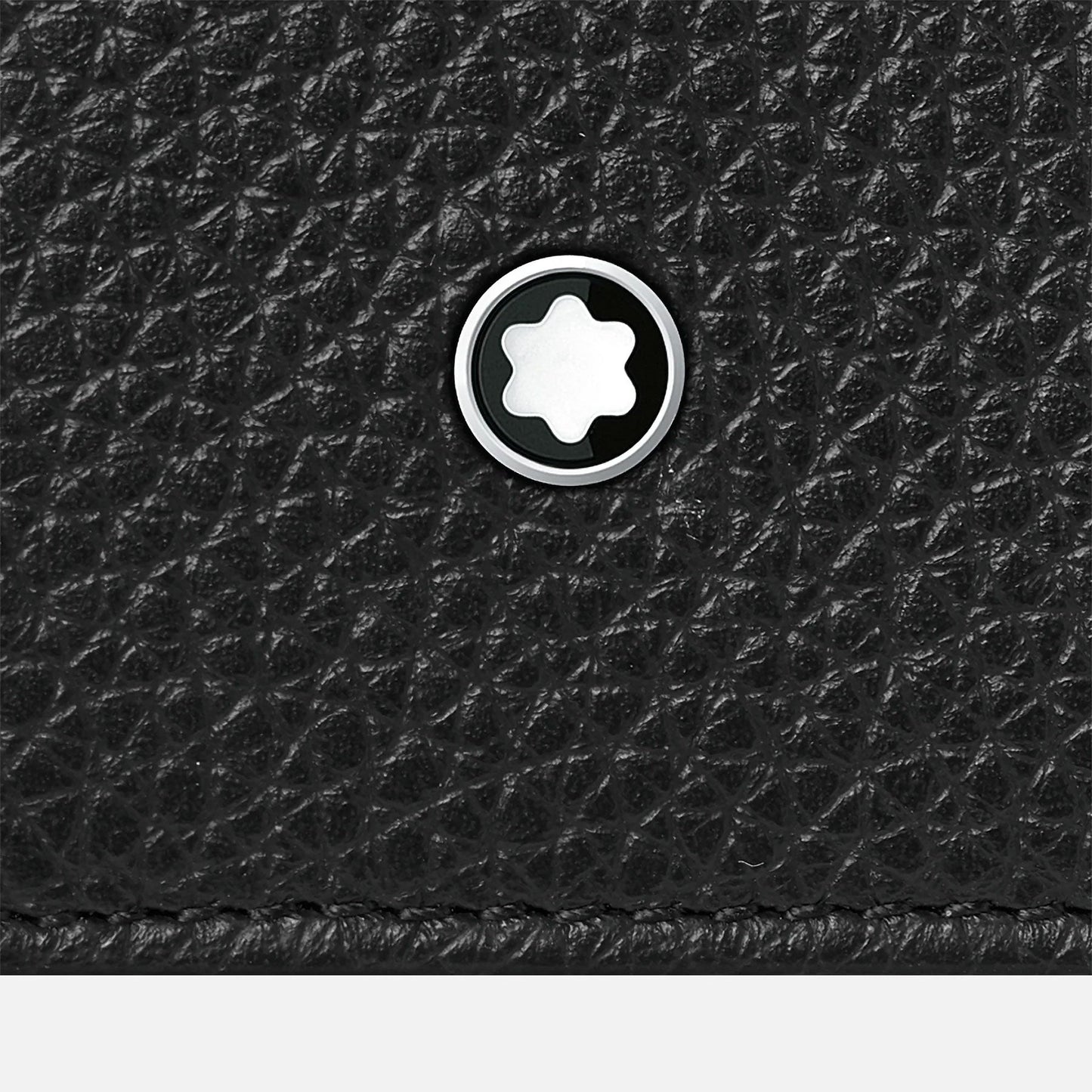 Close-up of the textured black leather surface of the Montblanc Meisterstuck Soft Grain Leather Business Card Holder with Bill Compartment, showcasing a circular metal emblem with a white star design at its center, reflecting Montblanc's craftsmanship.