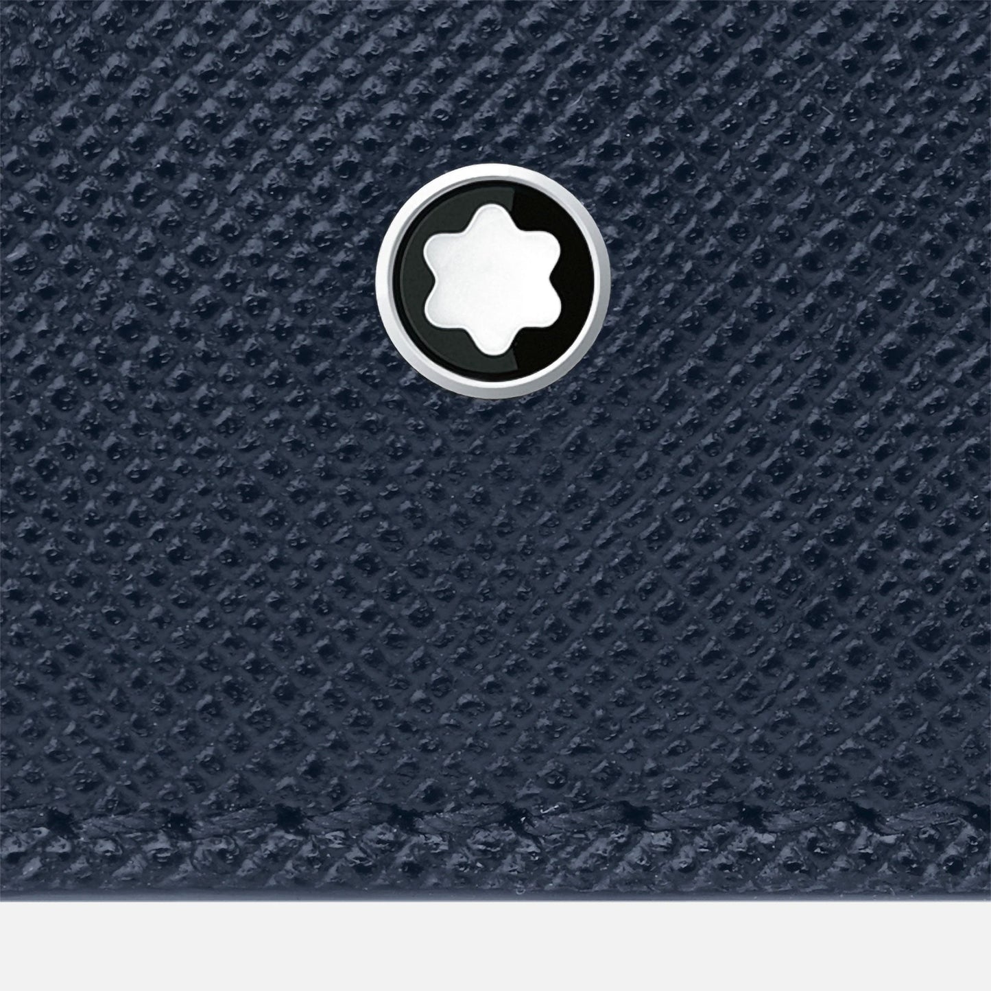 Close-up of a textured dark blue Saffiano leather surface on the Montblanc Sartorial Leather Wallet 6cc, adorned with a silver and black circular emblem with a star-shaped design in the center. This elegant piece is part of the distinguished Montblanc brand's Sartorial Collection.