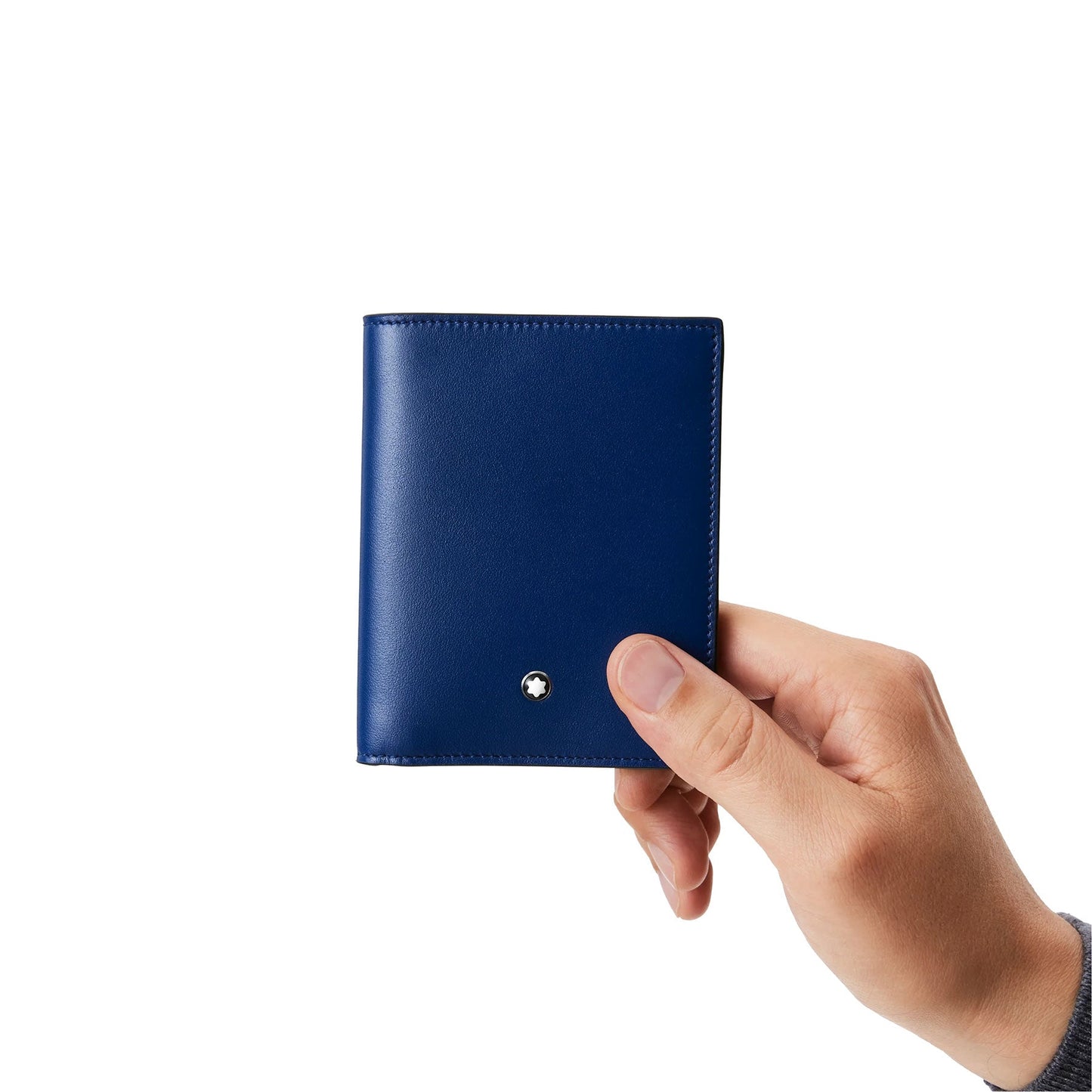 A hand holding a compact blue wallet against a white background. This Montblanc Meisterstück Compact Leather Wallet 6cc, Style Number 129678, showcases minimalist stitching and a small circular emblem on the front.