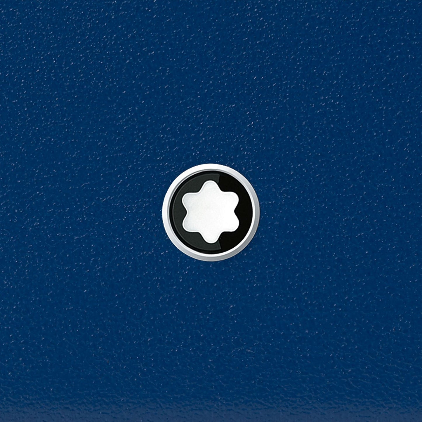 The image showcases the Montblanc Meisterstück Blue Leather Pocket 3CC Card Holder, featuring a textured blue surface. At its center is a circular emblem with a white star-like shape set against a black backdrop, all encased in a sleek silver ring. This striking design embodies the elegance of Montblanc's sophisticated craftsmanship.