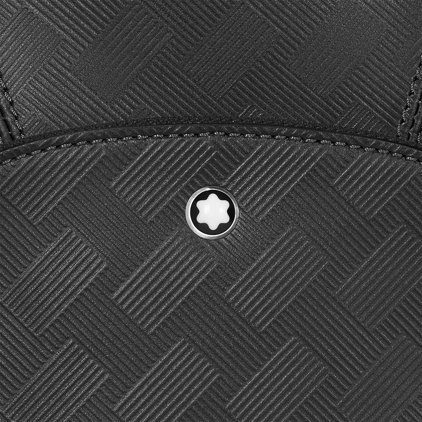 Close-up of the Montblanc Extreme 3.0 Black Leather Sling Bag, showcasing a black textured material with a subtle woven pattern reminiscent of full-grain leather. It is adorned with a small, round emblem featuring a white star-like shape in the center. The edges are meticulously stitched with black thread, enhancing the elegance of this Montblanc design.