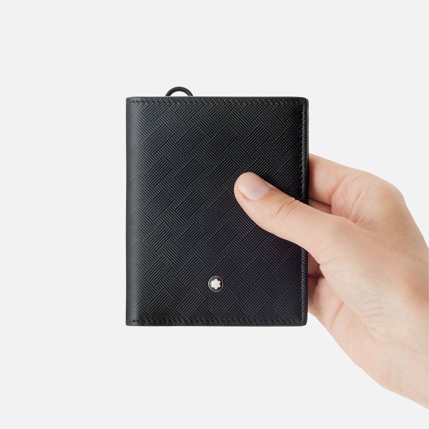 A hand holding a Montblanc Extreme 3.0 Compact Leather Wallet 6cc against a white background. The wallet, made of black leather, features a textured pattern and a small circular emblem near the bottom, epitomizing the elegance of the Montblanc brand.