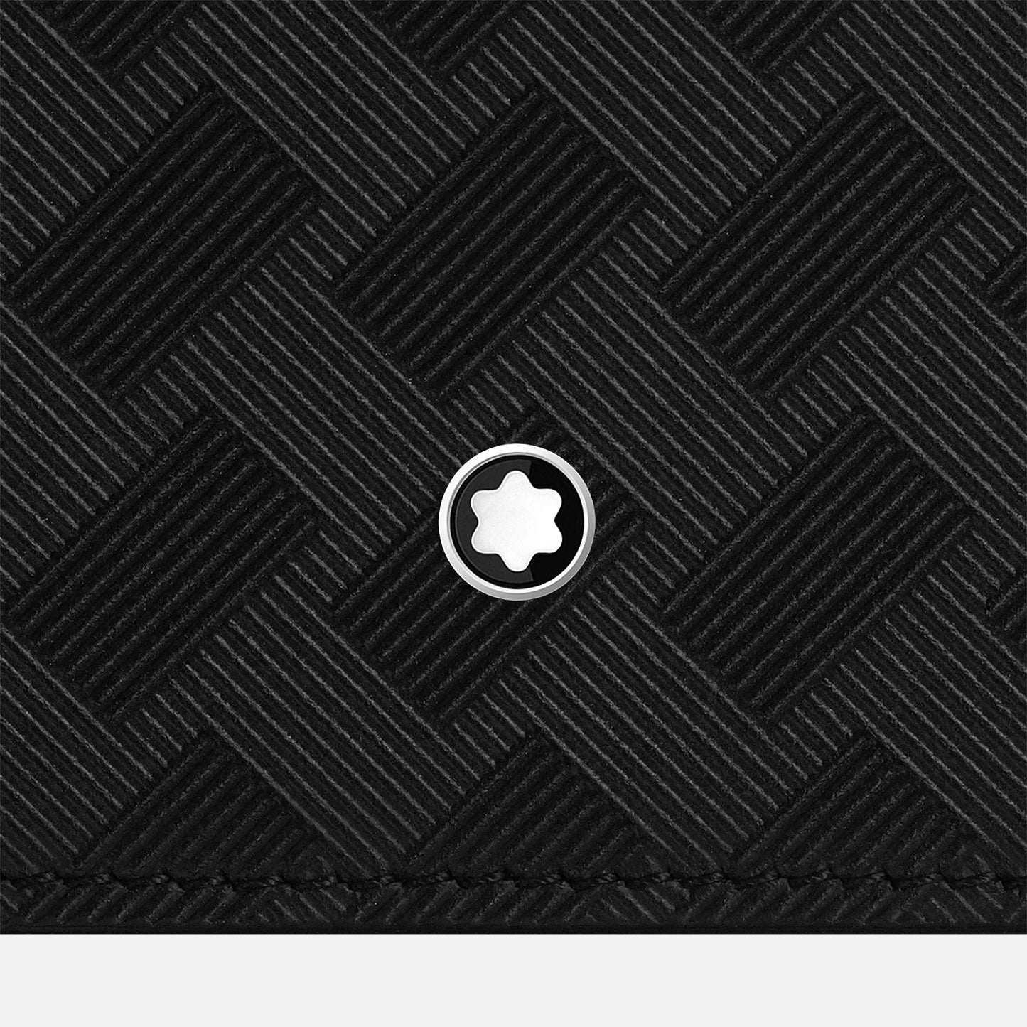 A close-up of a textured black surface with a woven pattern highlights a small circular white emblem featuring a star shape at the center. This image captures the elegance of Montblanc Extreme 3.0, often found in luxury accessories like the Montblanc leather card holder 6cc.