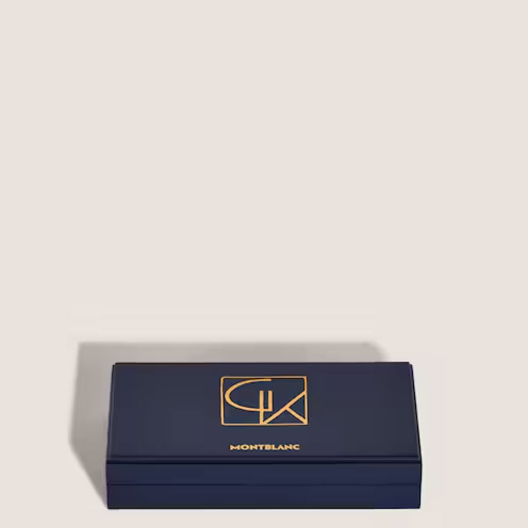 A Montblanc Masters Of Art Homage To Gustav Klimt Limited Edition Fountain Pen case in dark blue, adorned with a gold logo and lettering, is showcased on a light background. The sleek rectangular box boasts an elegant design inspired by the Vienna Secession, exuding luxury and sophistication.