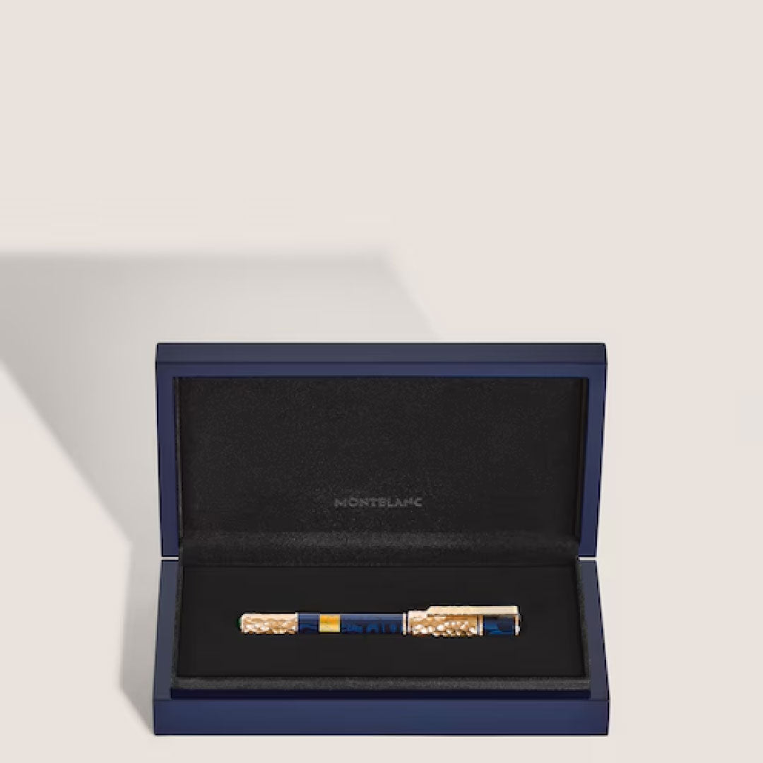 A Montblanc Masters Of Art Gustav Klimt Limited Edition Fountain Pen, featuring gold accents that evoke Gustav Klimt's opulent style, rests inside an open, elegant navy blue box with a black velvet interior.