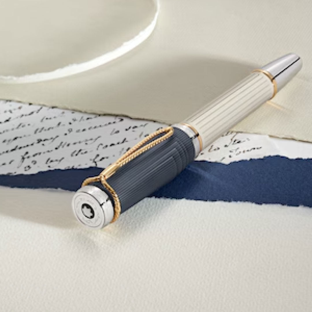 A Montblanc Writers Edition Homage to Jane Austen Limited Edition Fountain Pen, featuring a luxurious white and black barrel with gold accents, rests on a white table. It is elegantly placed atop a torn piece of handwritten paper, evoking Regency-era correspondence, set against a contrasting deep blue strip.