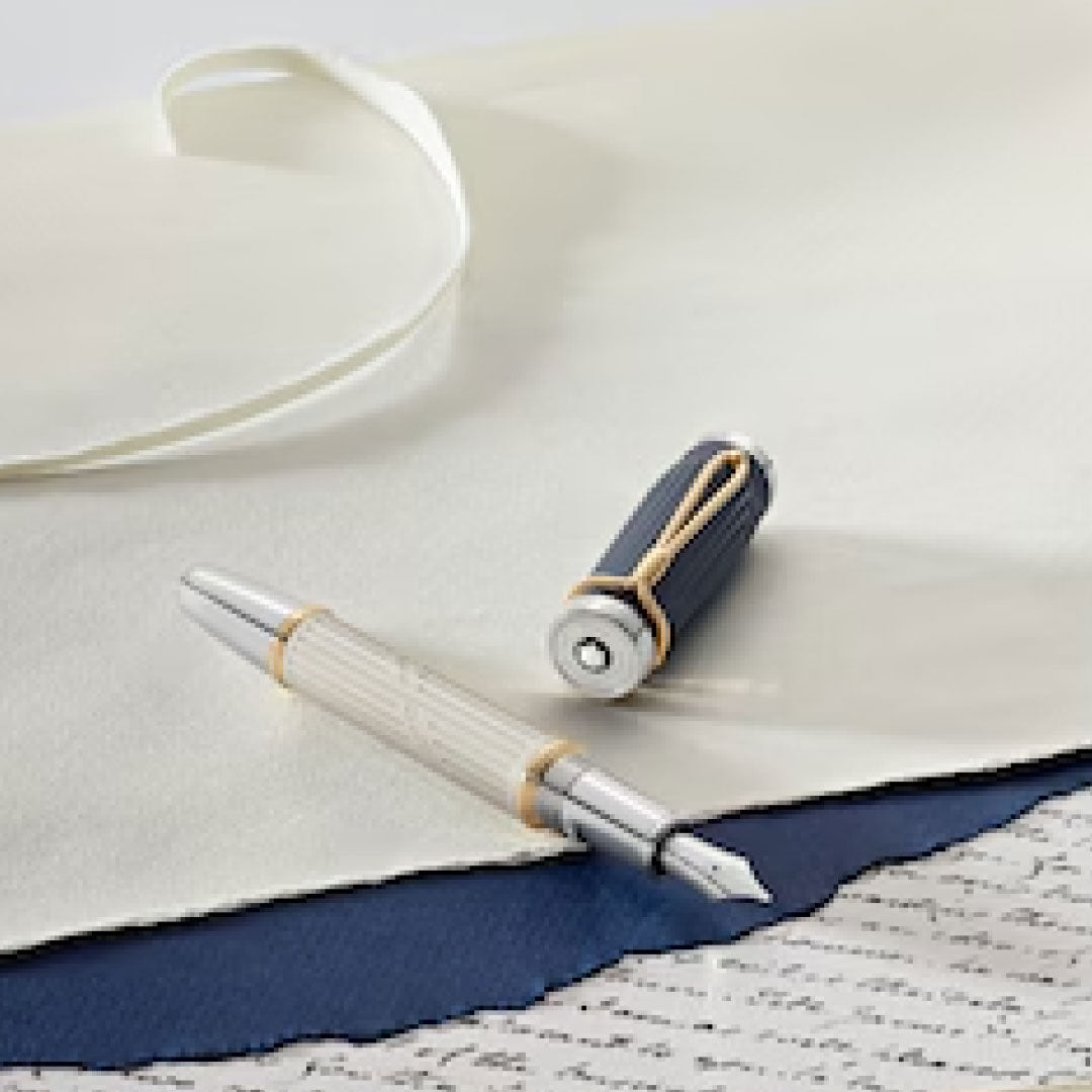 The Montblanc Writers Edition Homage to Jane Austen Limited Edition Fountain Pen, featuring a silver nib and a dark cap, rests on pieces of paper, one adorned with handwriting that echoes the style of Jane Austen. Beside the papers lies a white ribbon, embodying the sophisticated elegance characteristic of the Regency era.