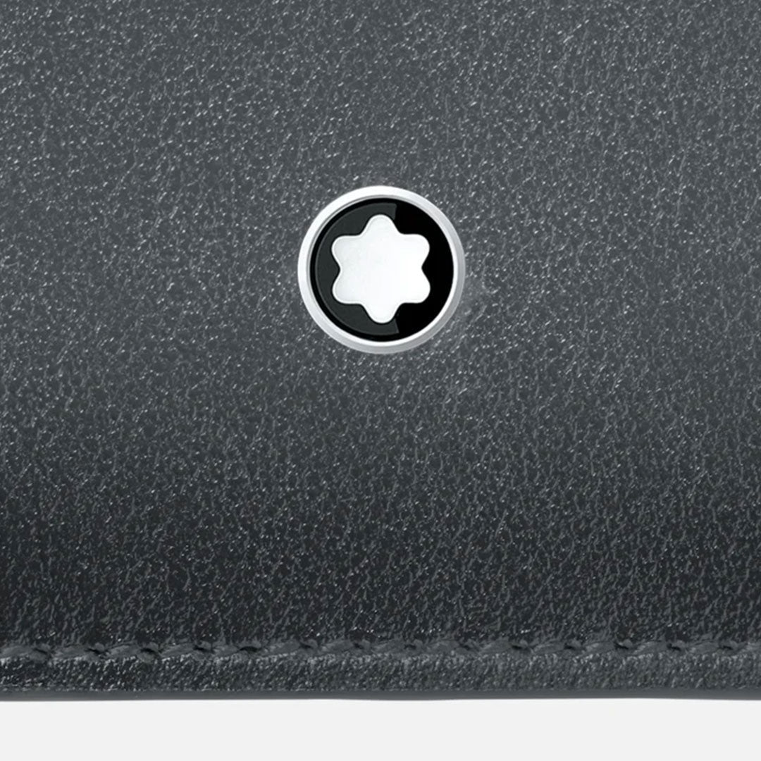 Close-up of a textured gray surface with a circular metal Montblanc logo featuring a white six-pointed star in the center. The lower edge shows detailed stitching, suggesting it may be crafted from high-quality leather, reminiscent of the elegance seen in the Meisterstück 6CC Black Leather Card Holder.