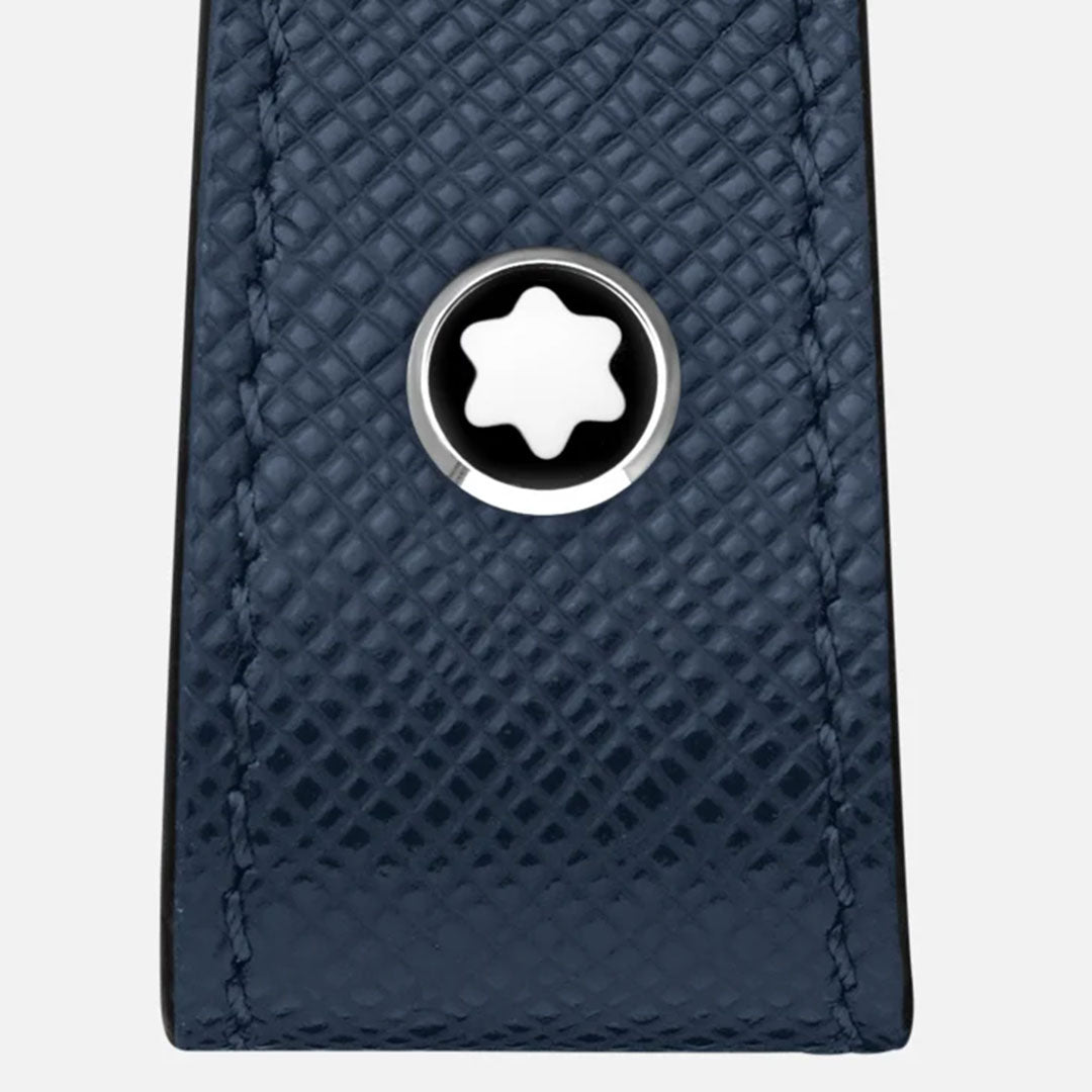 A detailed view of the Montblanc Blue Sartorial Loop Key Fob showcases its textured full-grain ink blue leather, adorned with a silver circular emblem featuring a white star-like symbol at its center. The key fob's leather surface is designed with a grid of small diagonal lines and includes a sleek detachable ring.