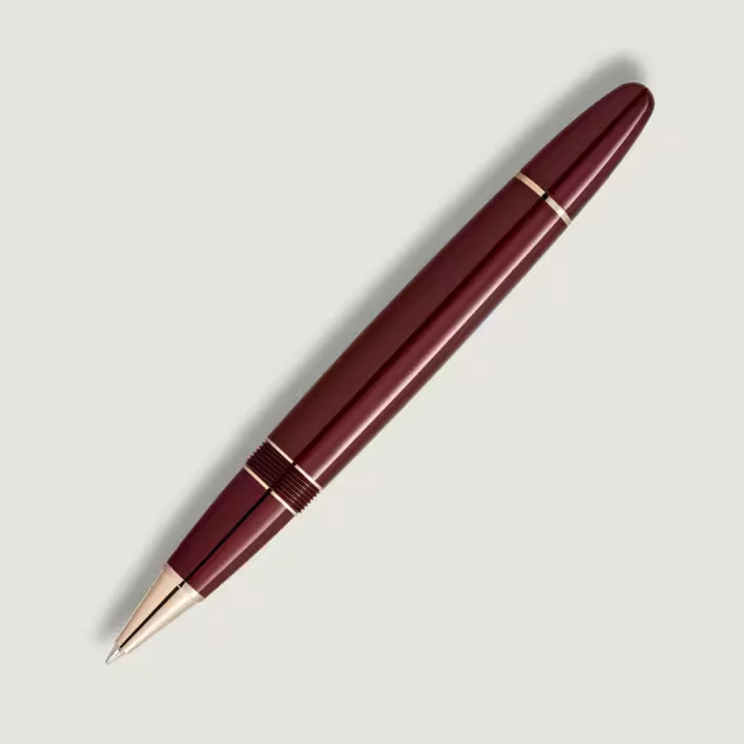 A Montblanc Meisterstück Burgundy Red Legrand Rollerball Pen with gold accents, shown diagonally on a light gray background. The pen features a smooth, glossy finish and a closed cap design.