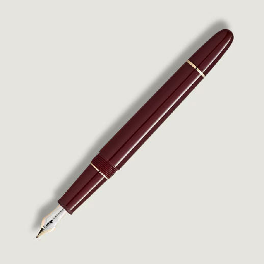 The Montblanc Meisterstuck Burgundy Red Classique Fountain Pen by Montblanc, featuring gold fittings and a silver nib, is displayed diagonally on a light gray background.