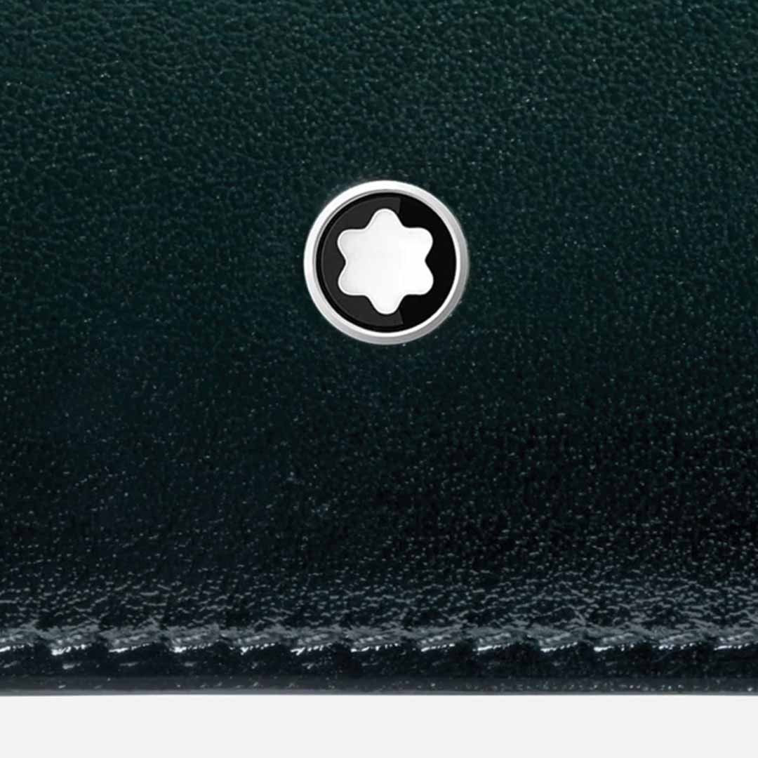 Close-up of a luxurious British green leather surface with a black and white circular emblem featuring a six-pointed star. The emblem, reminiscent of a capsule collection design, is centered on the Montblanc Meisterstück 6cc Leather Wallet, highlighting the intricate stitching on its textured surface.