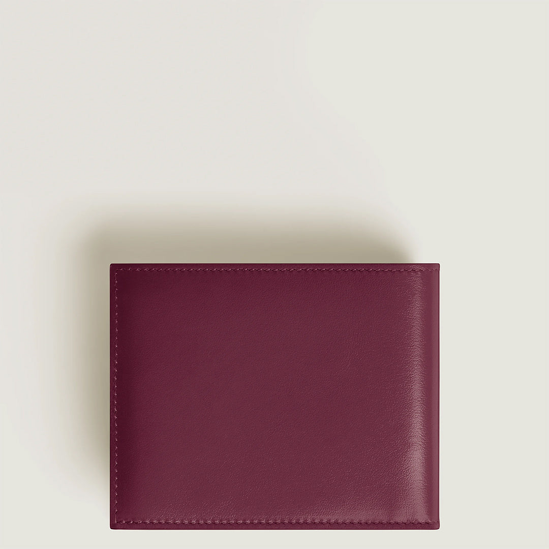 The Montblanc Meisterstück 6CC Wallet, a closed burgundy cassis leather wallet with no logos, rests on a light cream background. It features clean edges, a sleek finish, and discreet credit card slots that embody modern minimalist design.