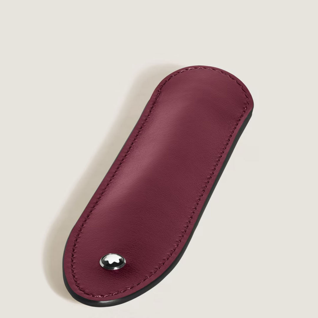 The Montblanc Meisterstuck 1 Pen Sleeve by Montblanc is a burgundy leather pen pouch with black edges, rounded at one end and pointed at the other, featuring a small metallic emblem near the tip on a light beige background.