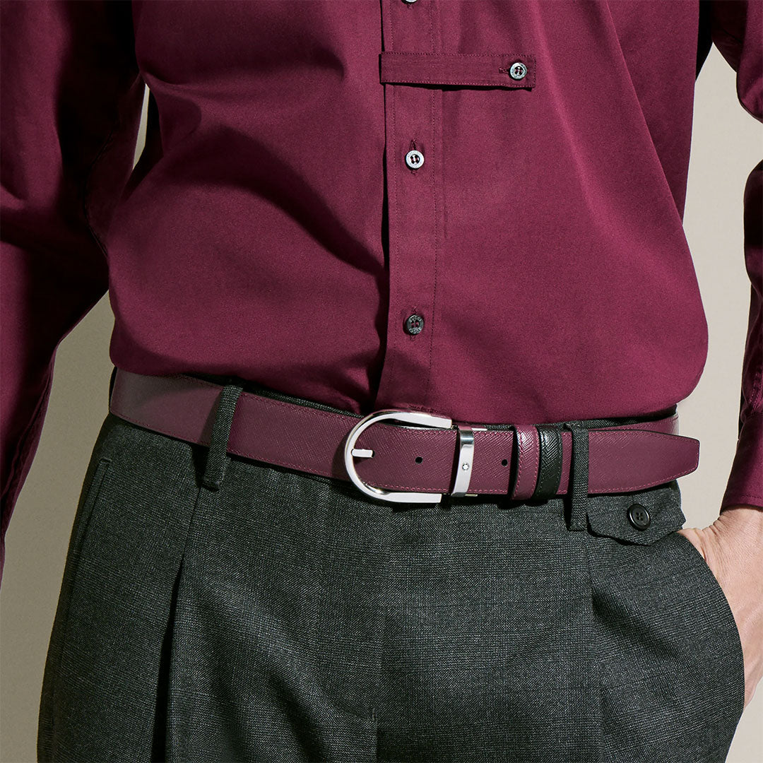 A person wears a burgundy button-up shirt with gray dress pants, accessorized by a Montblanc Horseshoe Buckle 35mm Reversible Leather Belt. Only their torso and waist are visible.