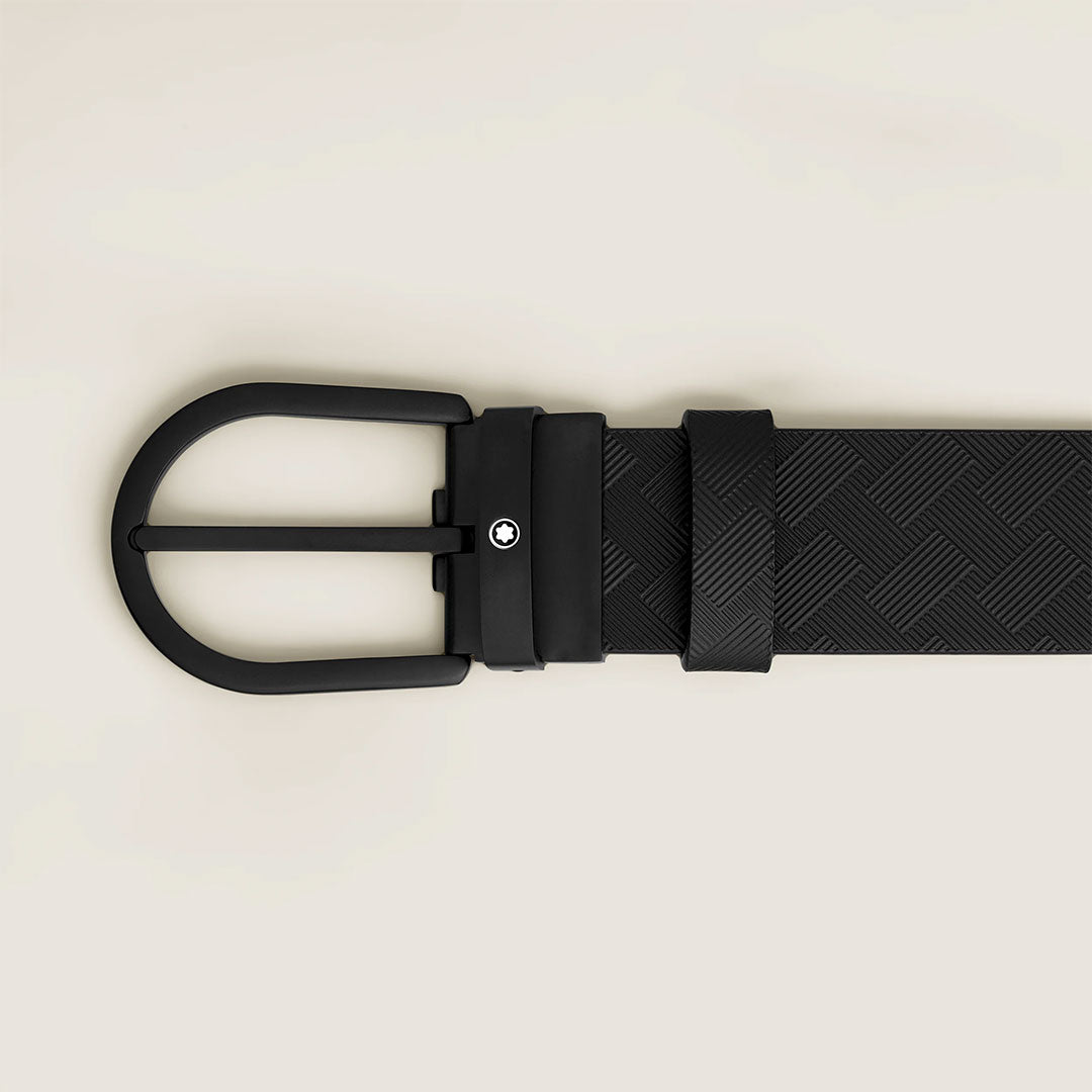 The Montblanc 35mm Black Leather Belt showcases supple black leather, a matte black buckle, and a subtle round emblem near the clasp—all elegantly set against a light beige background.