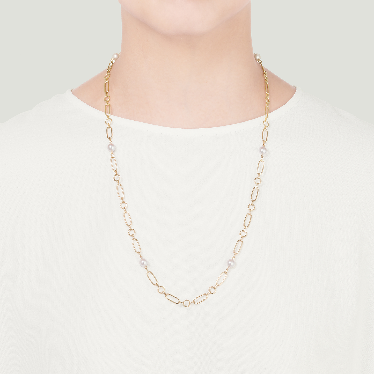 A person wearing the elegant Mikimoto M Code 18K Yellow Gold Akoya Cultured Pearl Station Necklace over a white shirt, with a plain, neutral background emphasizing the beauty of the necklace.