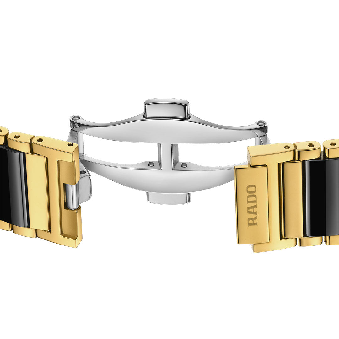 A close-up of the RADO Integral Quartz 31.5mm Watch shows a two-tone gold and black stainless steel bracelet with "RADO" engraved on a gold link. The silver clasp is partially open, revealing its mechanism.