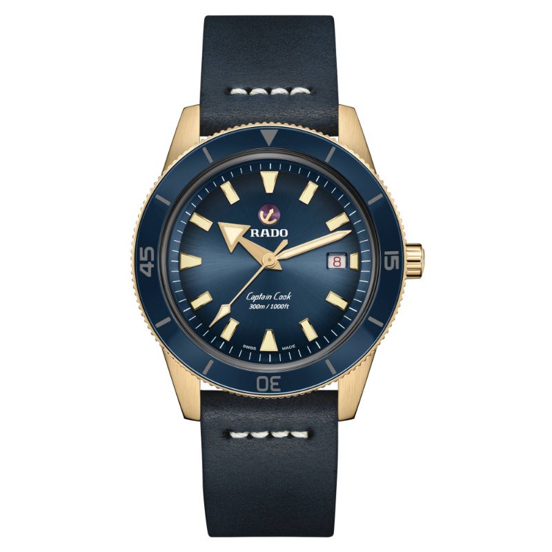 The RADO Captain Cook Automatic Bronze 42mm Watch showcases a captivating gold-tone case paired with a blue face. It is equipped with prominent luminous markers and includes a date window at the 3 o'clock position, complemented by a black leather strap. The bezel features minute markings, with RADO's iconic logo elegantly situated below the 12 o'clock marker.