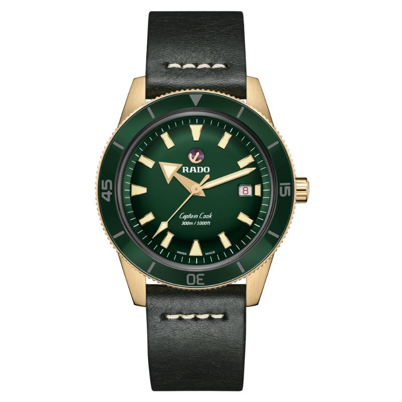 The RADO Captain Cook Automatic Bronze 42mm Watch boasts a luxurious gold-tone case with a striking green dial. It is equipped with a rotating bezel, bold hour markers, luminescent hands, and features a date display at 3 o'clock. The watch is elegantly paired with a black leather strap accented with white stitching, exuding timeless sophistication.